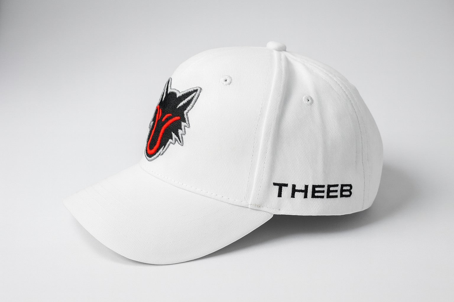 My Store white baseball cap with embroidered black and red wolf head logo and THEEB text on the side.