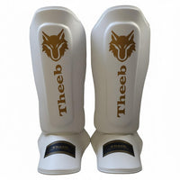 My StoreHere youth shin guards in white genuine cowhide leather with gold Theeb logo and lettering. Ideal for Muay Thai, MMA, and sparring.